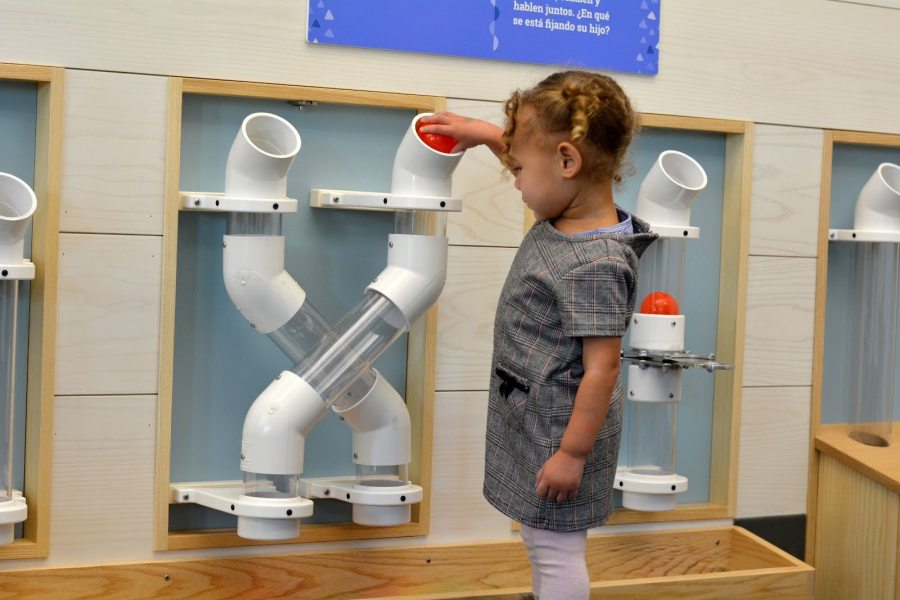 A toddler picks up a ball and puts it through a tube.